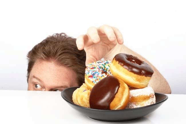 A man holding a tray of donuts and smiling while posing for a food photo.