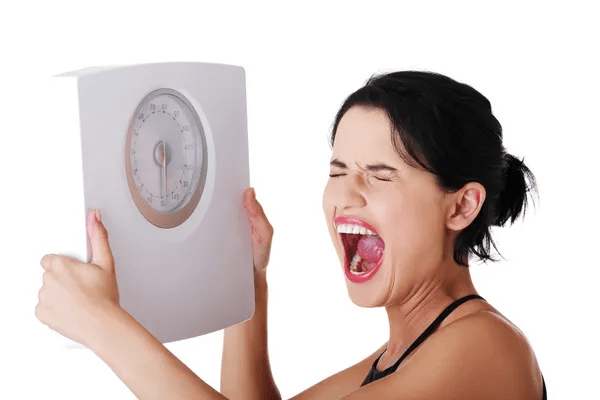 A woman holding a scale and smiling as a symbol of weight loss progress.